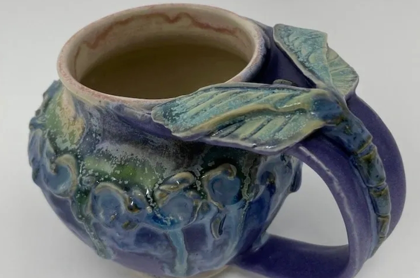 A cup with leaves on the handle and a mug in it.
